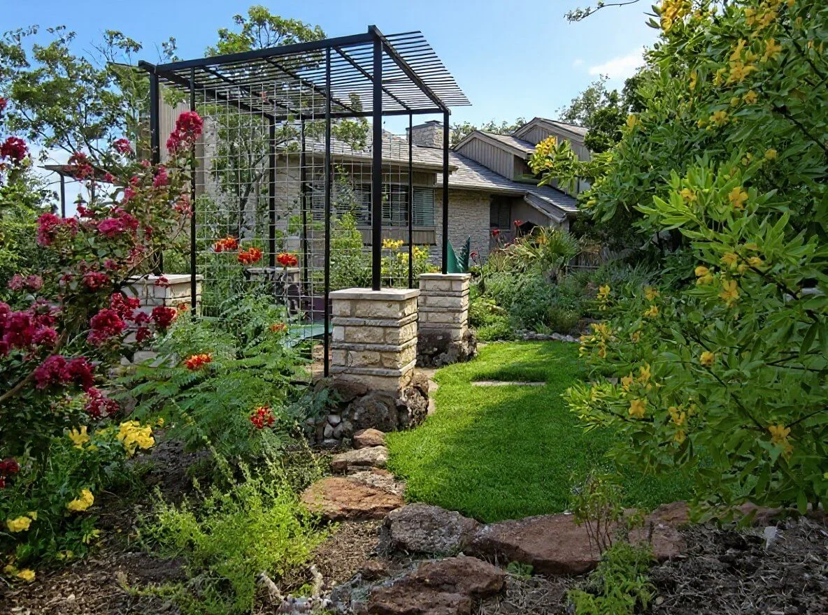 Custom metal arbor with stone pillars surrounded by lush garden landscaping